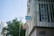 Signage on a building corner with metal bars covering windows. Blue and red signs display Chinese characters. Power lines stretch overhead, and there is a partial view of a modern building and trees in the background.
