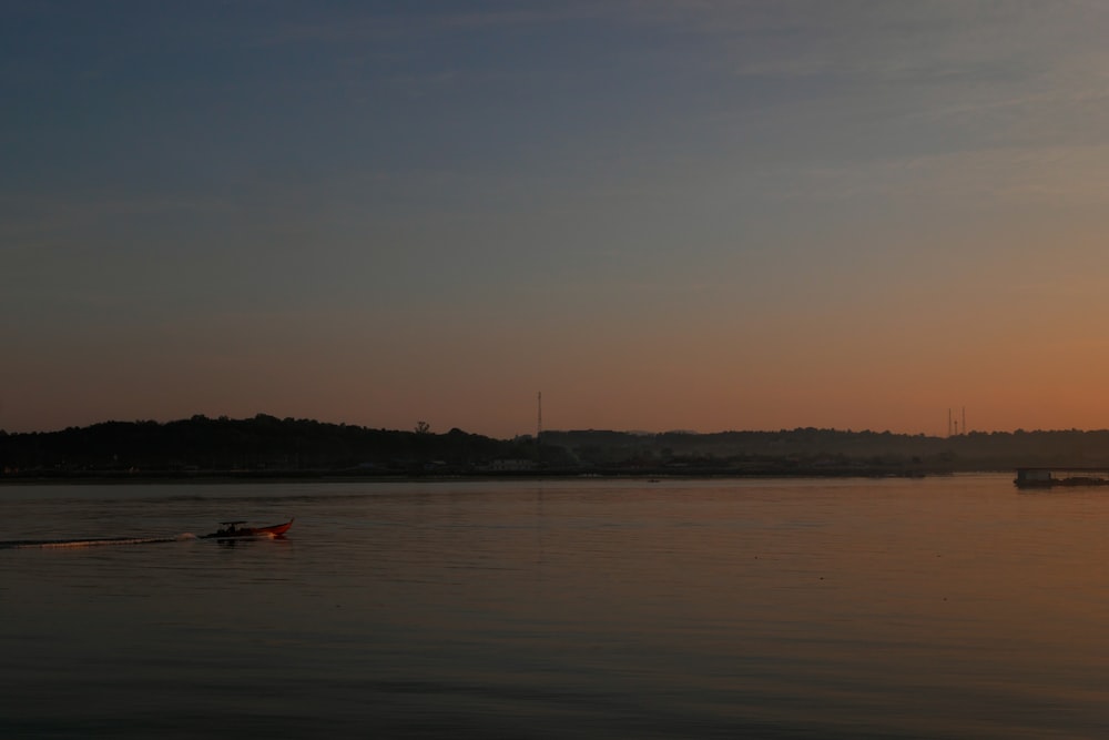 a boat floating on top of a lake at sunset