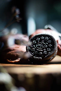 Close-up of a smooth, creamy cookies & cream chocolate square melting gently on a rustic wooden surface.