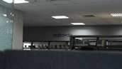 The image depicts an indoor space with bookshelves lined against a wall. The word 'multimedia' is visible on the far wall, indicating that this section could be related to multimedia resources. The ceiling has recessed lighting, and the overall tone of the space is modern and minimalistic.