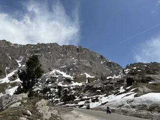 A rugged motorcycle winding through a narrow mountain pass with snow-capped peaks in the background.