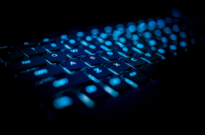Close-up photo of a sleek mechanical keyboard with blue backlighting in a dark tech workspace.