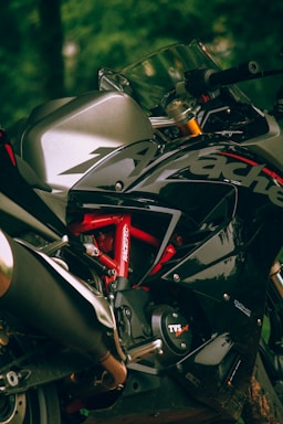A close-up view of a sleek and sporty motorcycle, focusing on the chassis and branding details. The motorcycle features a metallic silver and glossy black color scheme with red accents. The design emphasizes its aerodynamic and powerful look.