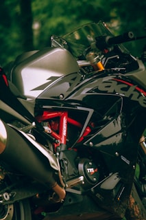 A close-up view of a sleek and sporty motorcycle, focusing on the chassis and branding details. The motorcycle features a metallic silver and glossy black color scheme with red accents. The design emphasizes its aerodynamic and powerful look.