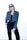 A person with short, light brown hair wears oversized dark sunglasses and a stylish outfit consisting of a blue-grey blazer over a black top and black trousers. The person has one hand in their pocket and exudes a confident demeanor against a bright, minimalist background.