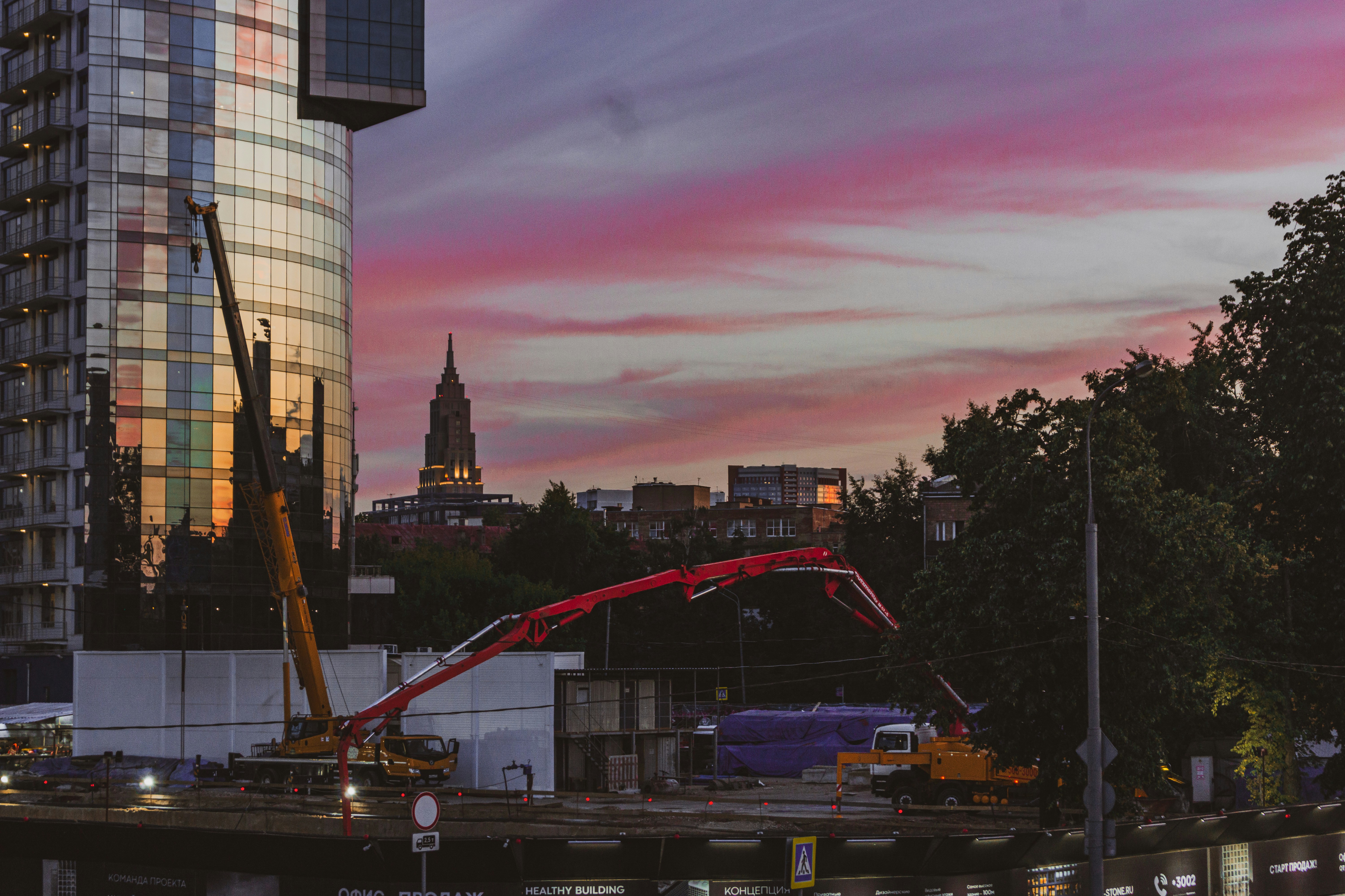 Red concrete pump boom unfolded beside a tower at dusk