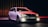 A sleek and modern BMW station wagon is parked under dramatic lighting. The car's headlights are on, creating a powerful contrast against the dark background. The reflective surface of the vehicle captures red and blue lighting accents, emphasizing its aerodynamic design.