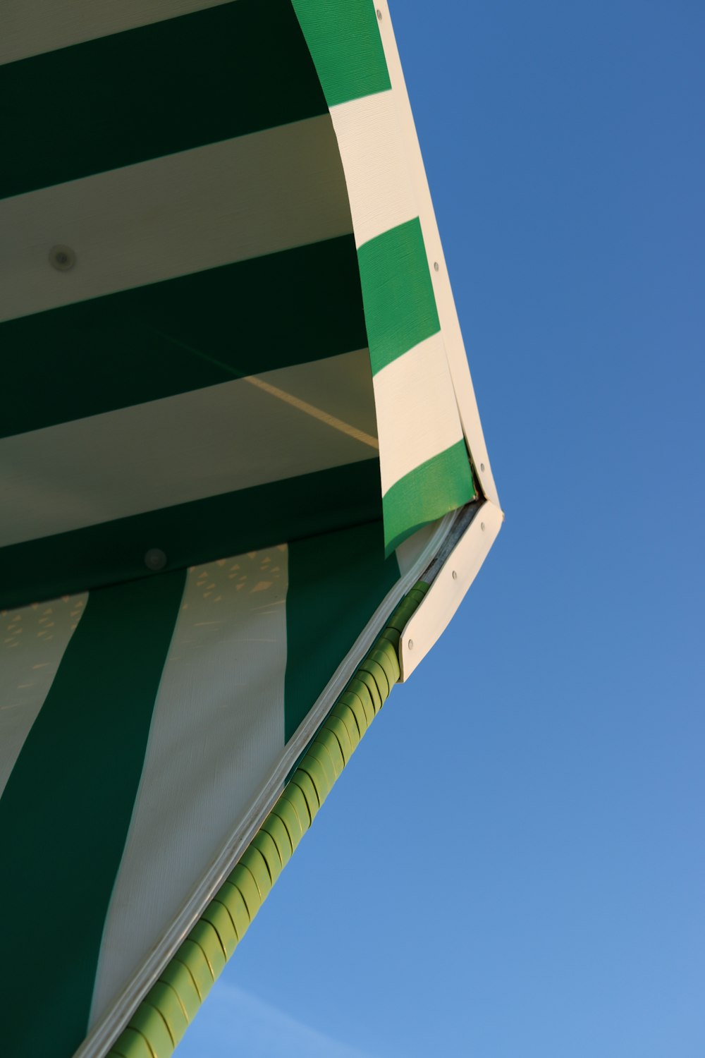 a green and white striped umbrella against a blue sky