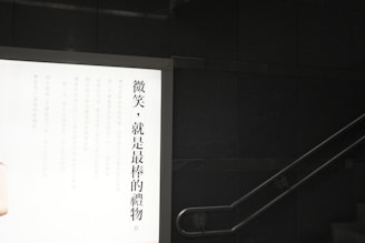 A wall-mounted illuminated advertisement display with Chinese text on the left side against a dark wall. A staircase is visible on the right with a metal handrail.