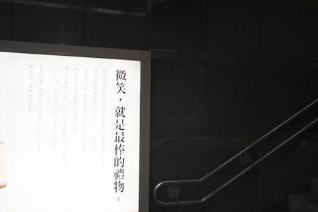 A wall-mounted illuminated advertisement display with Chinese text on the left side against a dark wall. A staircase is visible on the right with a metal handrail.