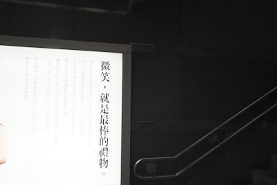 A wall-mounted illuminated advertisement display with Chinese text on the left side against a dark wall. A staircase is visible on the right with a metal handrail.