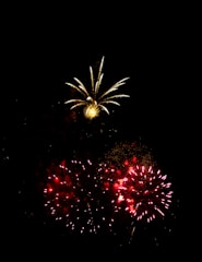 A vibrant display of fireworks lights up the night sky. Bright red and yellow bursts create a stunning contrast against the dark backdrop, with sparkles and trails enhancing the visual spectacle.