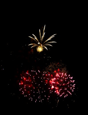 A vibrant display of fireworks lights up the night sky. Bright red and yellow bursts create a stunning contrast against the dark backdrop, with sparkles and trails enhancing the visual spectacle.