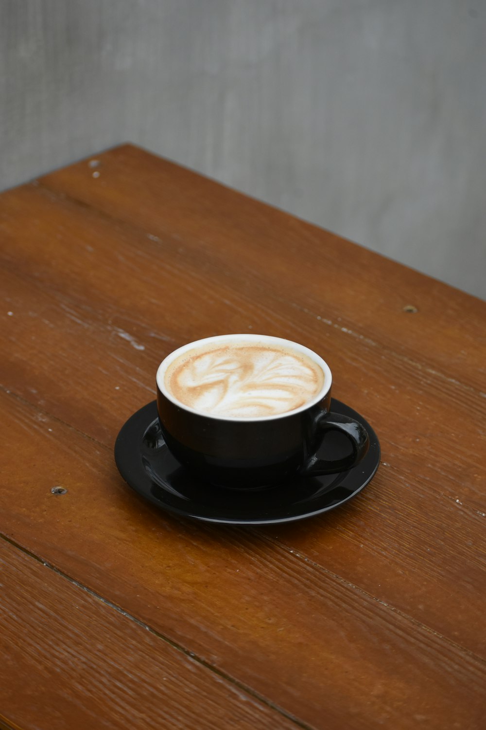 um cappuccino em um pires preto em uma mesa de madeira
