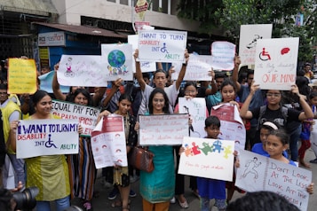 A group of people is gathered holding various signs and posters advocating for disability rights and empowerment. The signs carry messages promoting inclusivity, equal opportunities, and changing perceptions about disabilities. The crowd consists of diverse individuals, including children and adults.