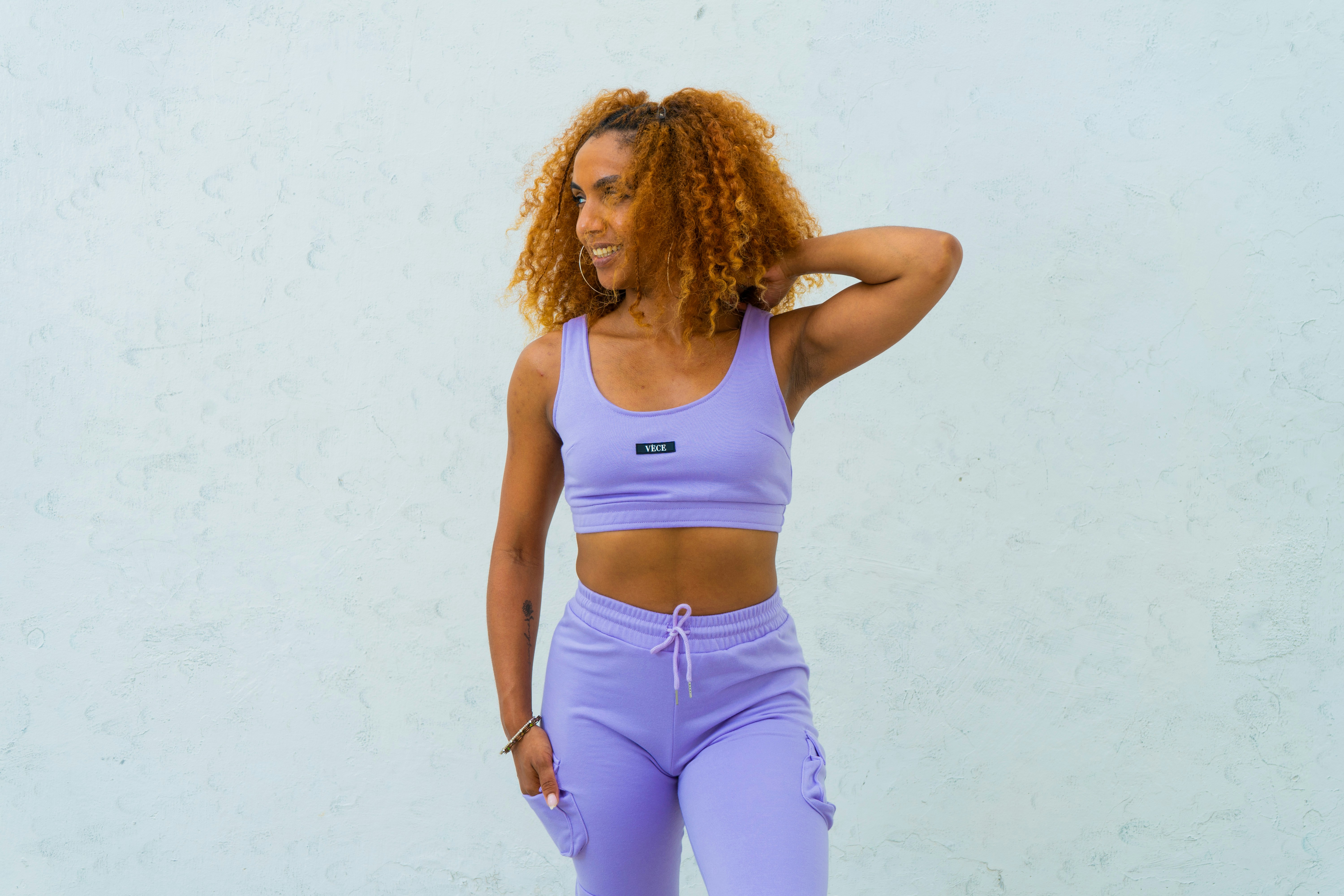 a woman with curly hair wearing a purple sports bra top and matching leggings