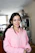 A smiling woman wearing a pastel pink blouse from Moon Ligdht LLC, standing in a sunlit room.
