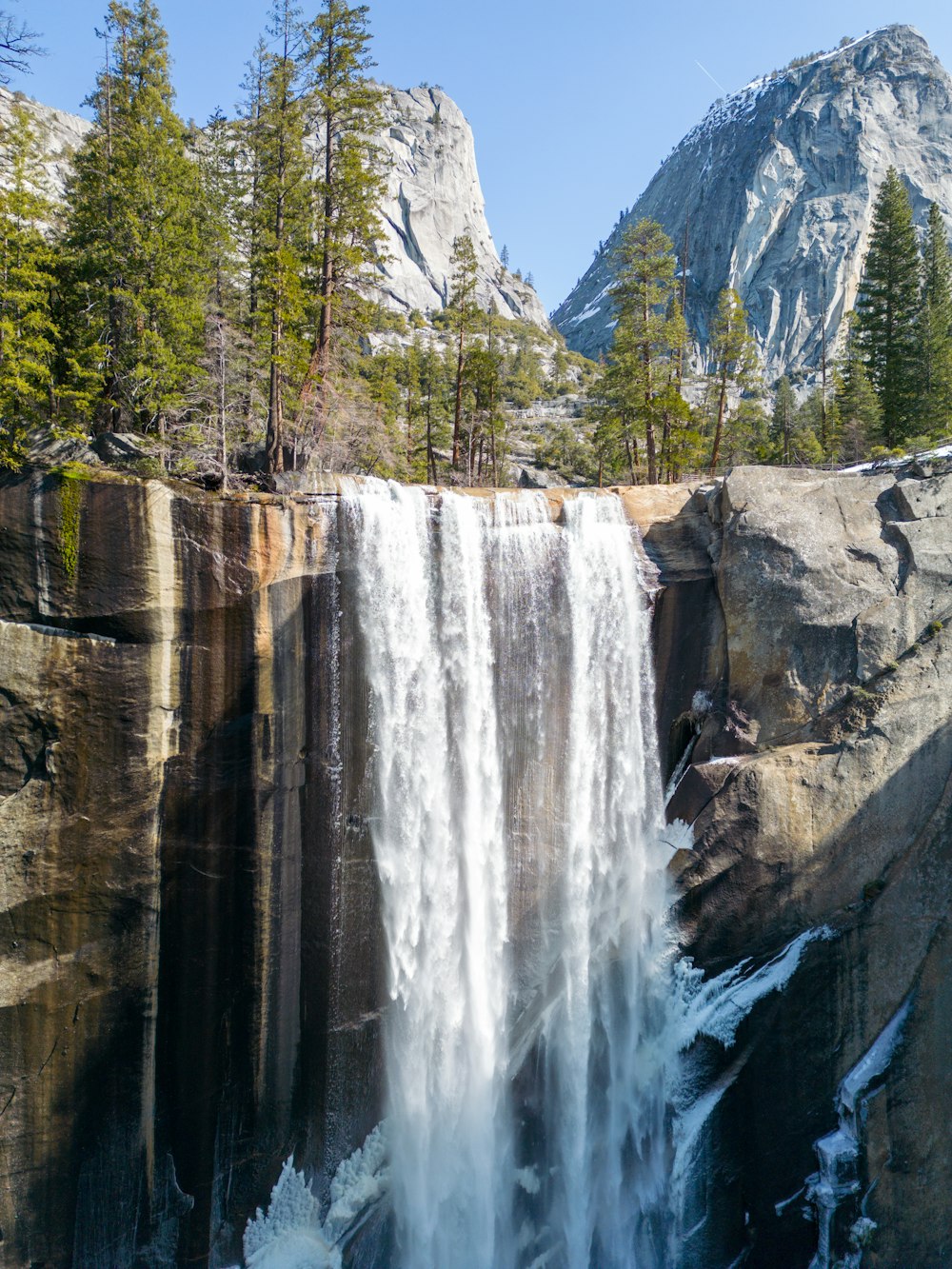 a large waterfall with trees and mountains in the background