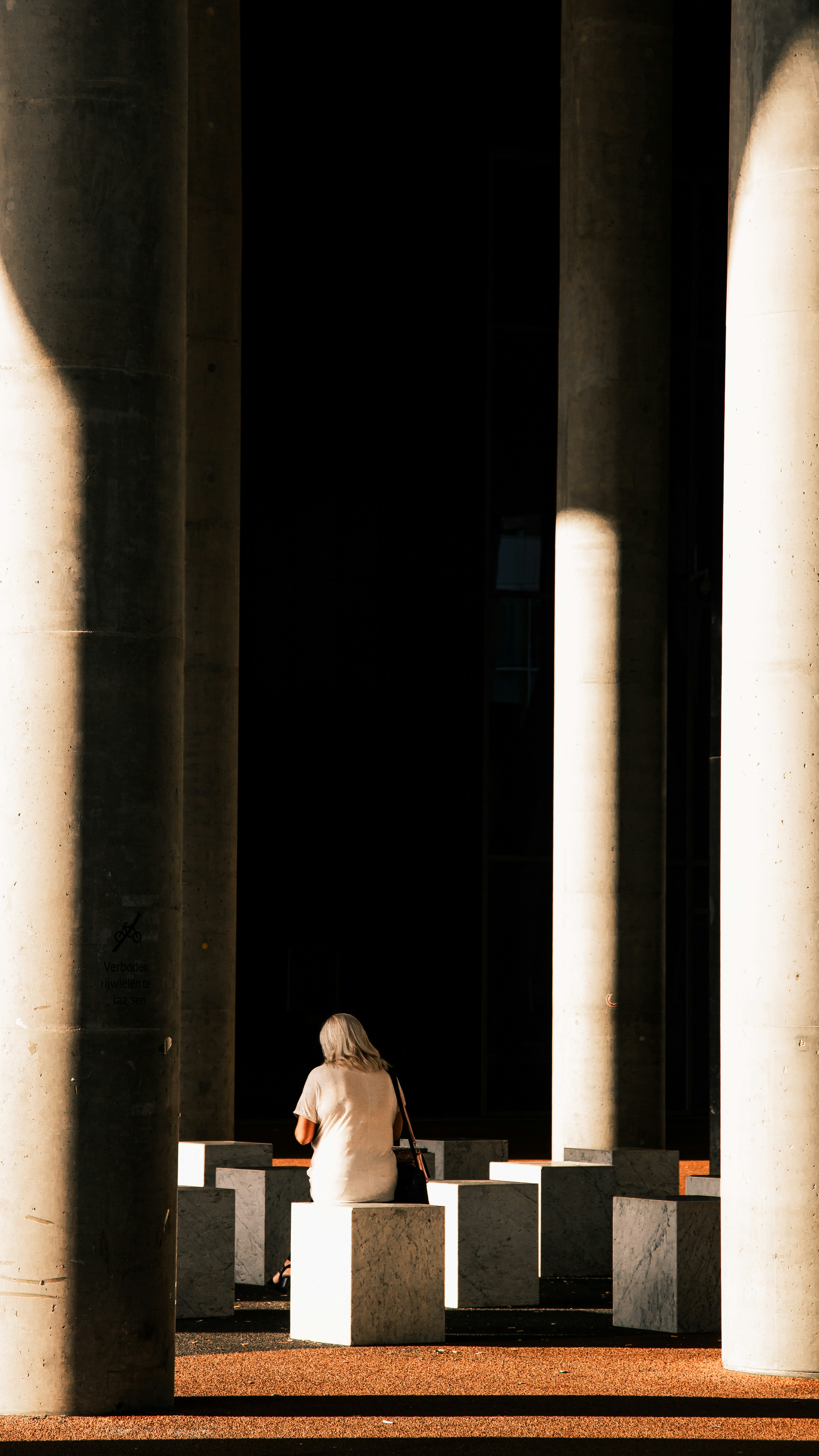 a person sitting on a bench under some pillars