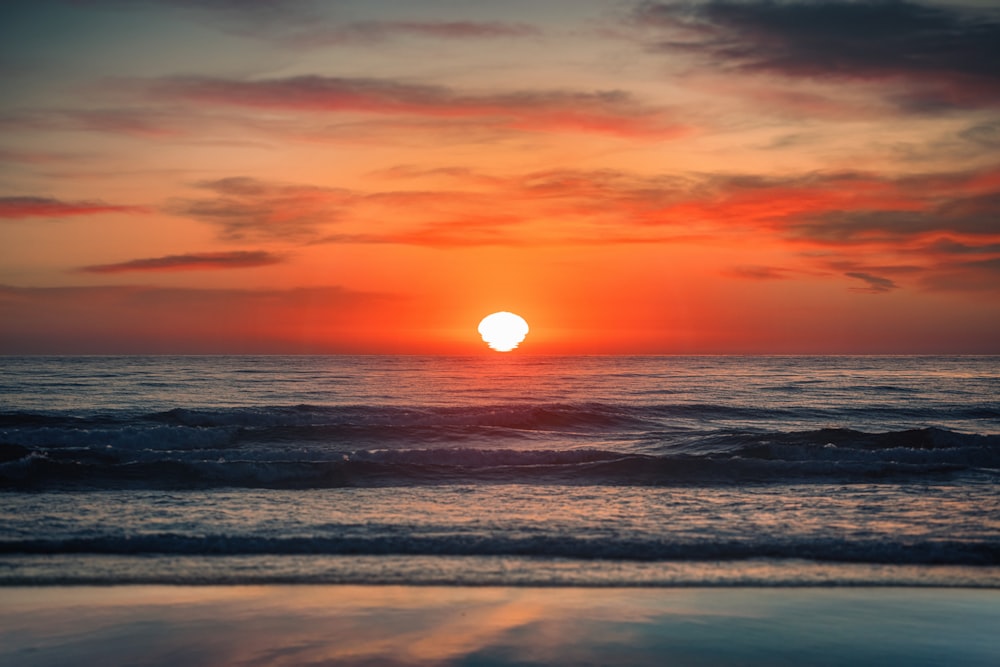 the sun is setting over the ocean on a cloudy day