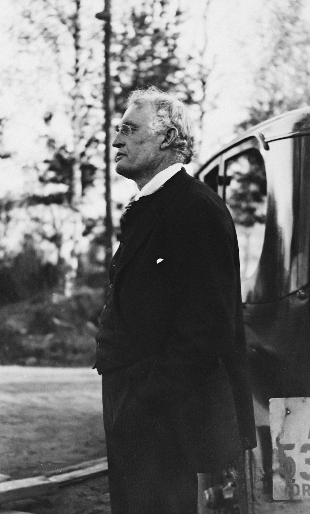 a black and white photo of a man standing next to a car