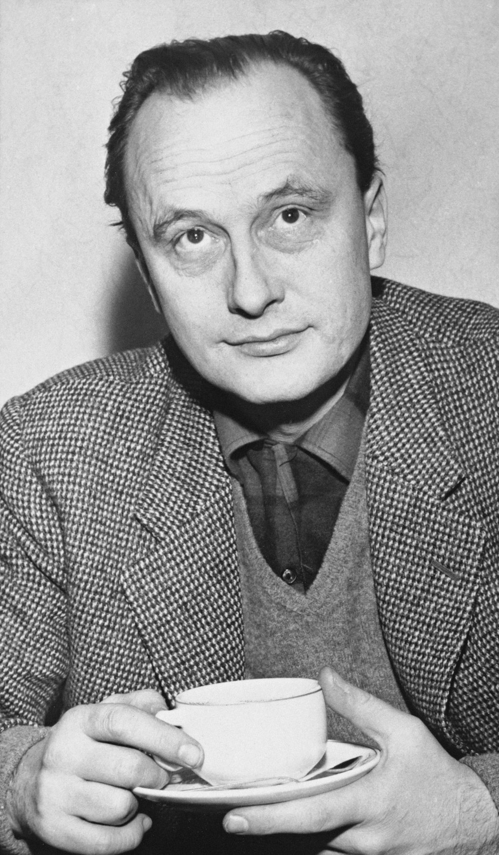 a black and white photo of a man holding a cup and saucer