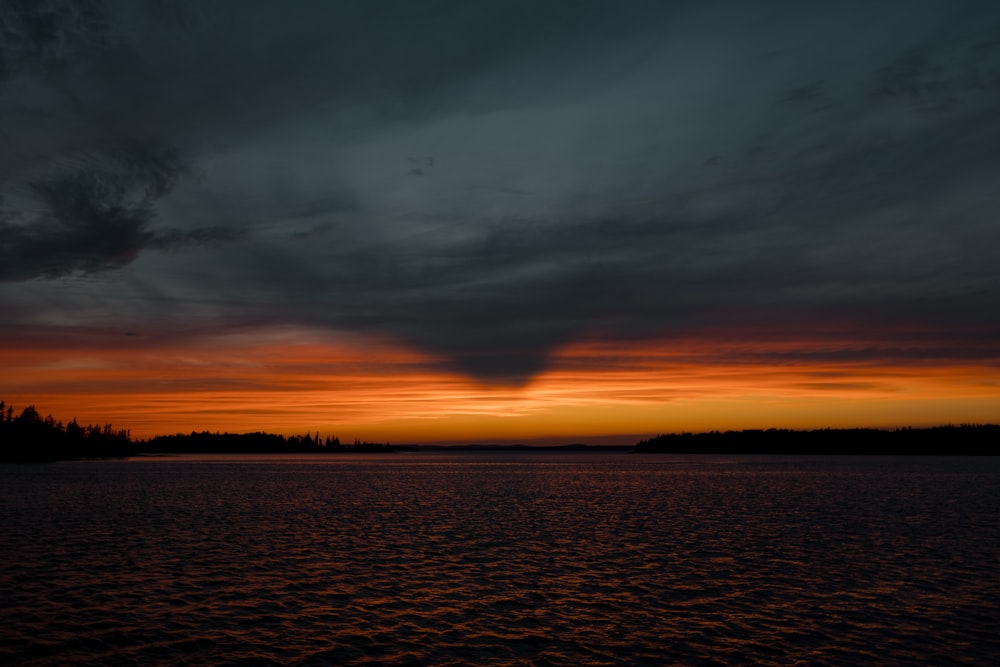 a sunset over a body of water with trees in the background