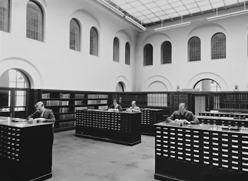 A cozy room filled with shelves of archival documents and members engrossed in their genealogical research.