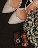 A pair of chic, modern shoes placed next to a small bouquet of fresh flowers on a light wooden floor.