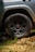 A close-up view of the rear wheel of a vehicle with 'TRD' branding on the hubcap, parked on a gravelly surface with some green grass. The wheel and tire show signs of dirt, suggesting off-road conditions.
