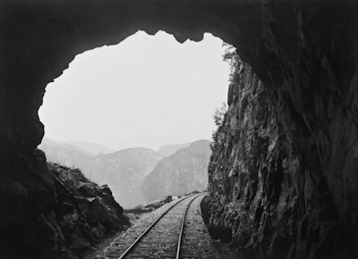 Railway tracks curving through a mountainous region with a tunnel entrance.