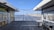 A wooden boardwalk leads to a scenic view of a sandy beach with a shoreline and distant buildings. The sky is clear and blue. On either side of the walkway, there are small food stalls with brightly colored signs, one offering Caribbean cuisine and another featuring seafood.