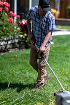 Gardener trimming bushes in a well-kept residential garden on a sunny day.