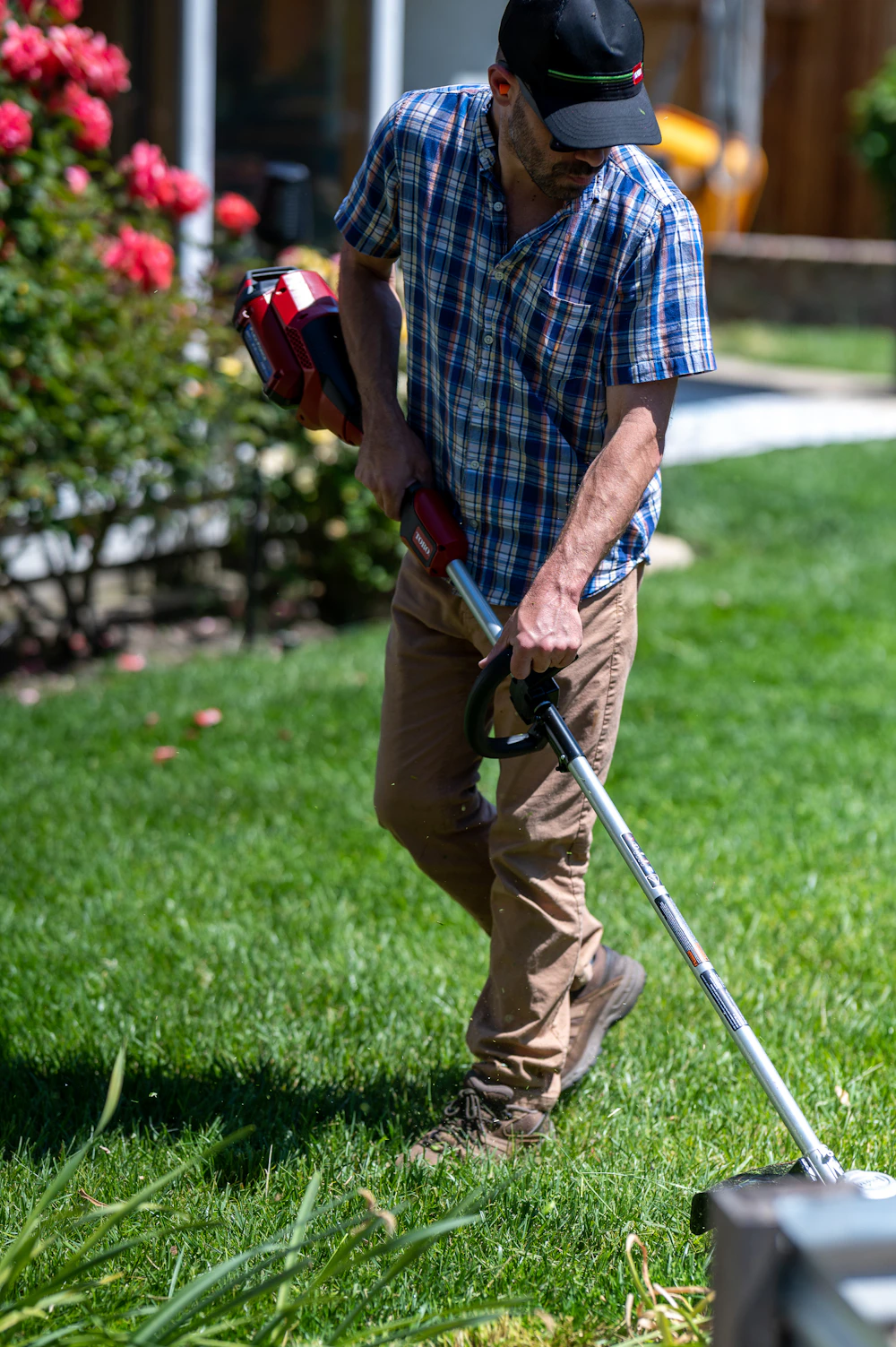 Crew member edging a green lawn with a battery trimmer on a sunny day