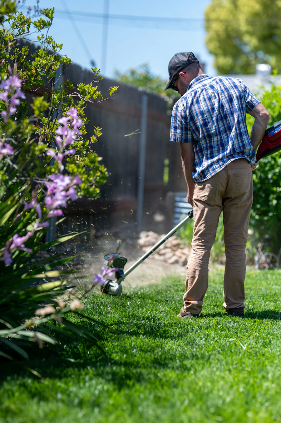 A landscaper mowing a lawn with a push mower in bright daylight
