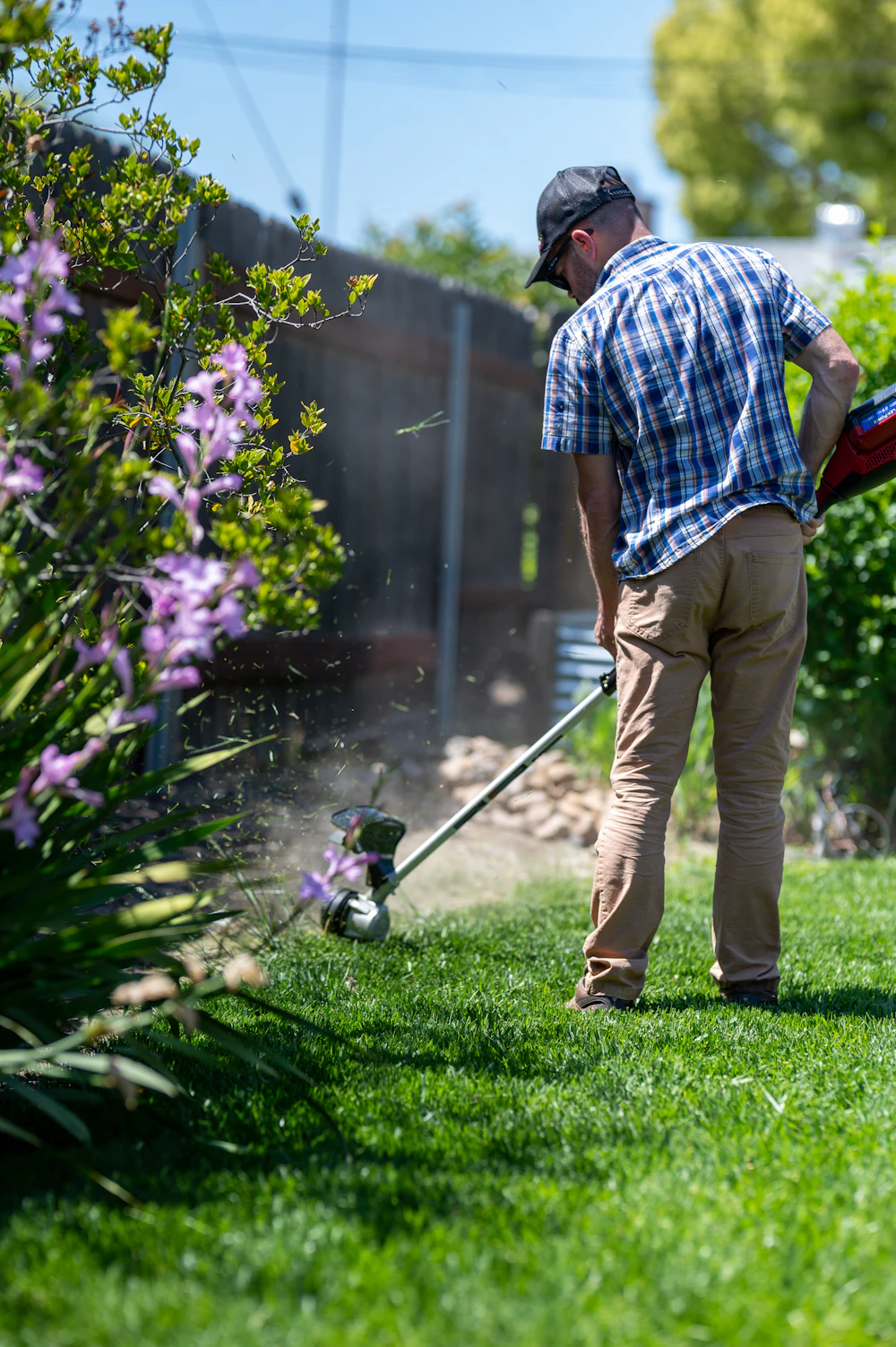 Landscaper edging a green lawn with a battery trimmer on a sunny day