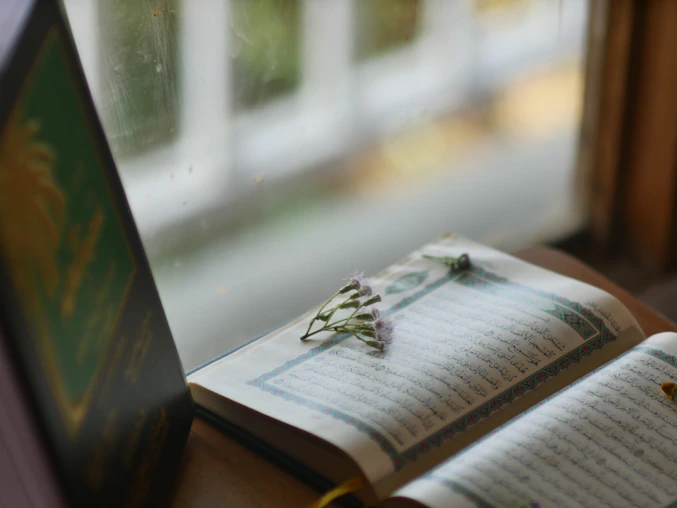 A peaceful study desk with an open Qur’an, a notebook, and a cup of tea by a window letting in soft natural light.