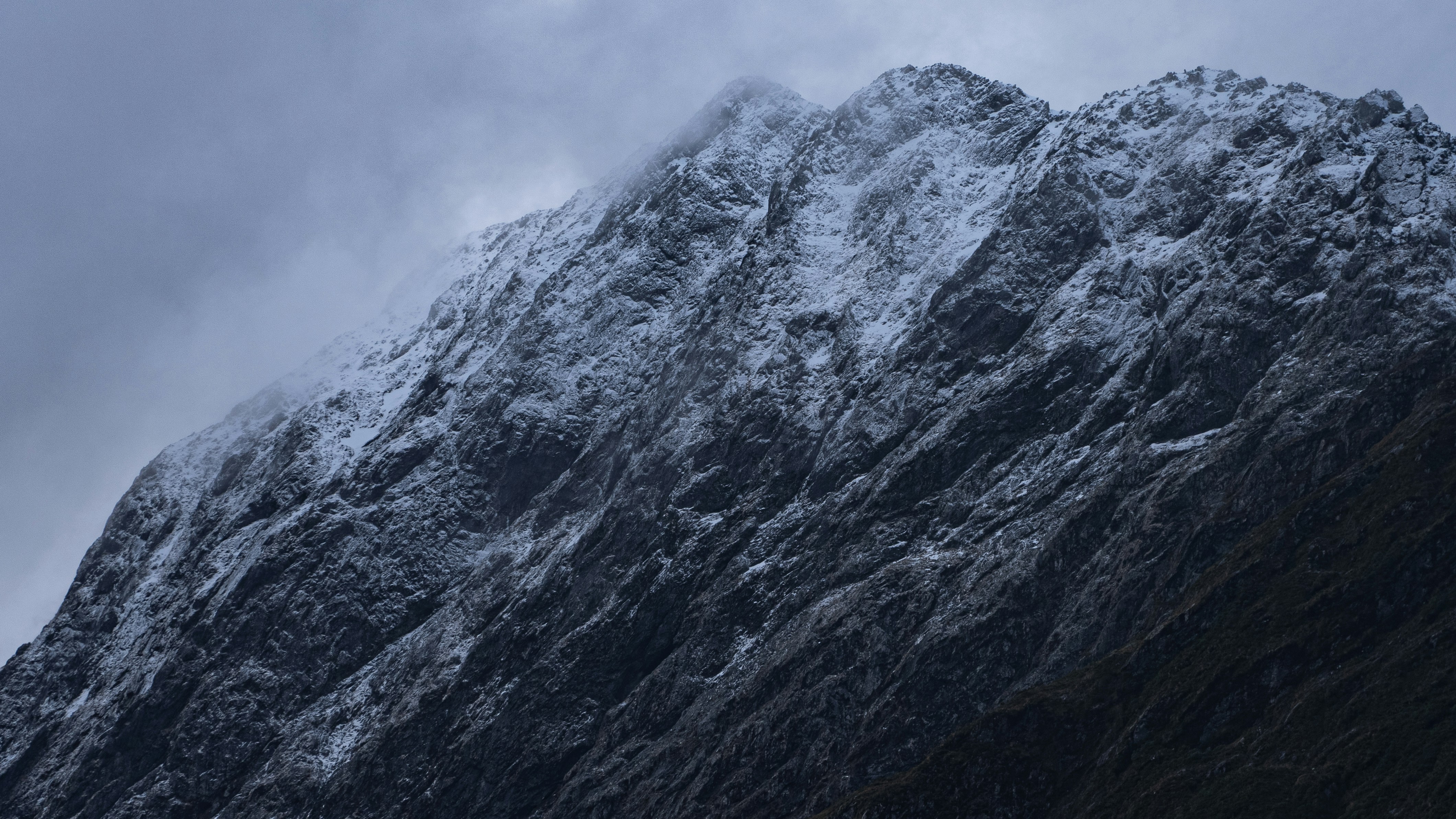 a very tall mountain covered in snow under a cloudy sky, Fresh Snow on mountain peak in Milford Sound, New Zealand. Clouds above mountain peak with snow. Snowfall on mountain.