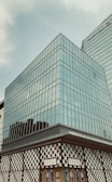 A modern glass building with a geometric facade, featuring large windows reflecting the sky. The lower section of the building displays the Gucci store front, characterized by a stylish pattern and clear branding.