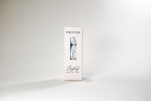 A package labeled 'Prestige' containing a single golf ball with the word 'Legacy' written on it. The packaging is white with a transparent section displaying the ball. The overall design is minimalist and sleek.