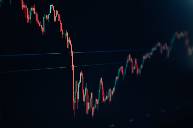 A financial chart displaying a downward trend with multiple sharp peaks and valleys. The chart features predominantly red and green candlesticks against a dark background, indicating fluctuations in market values.