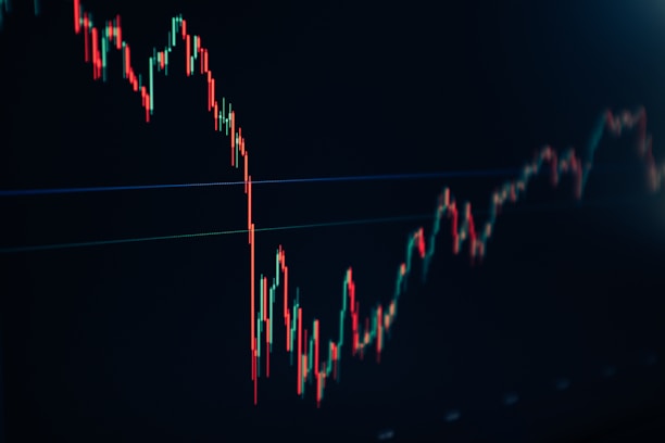 A financial chart displaying a downward trend with multiple sharp peaks and valleys. The chart features predominantly red and green candlesticks against a dark background, indicating fluctuations in market values.