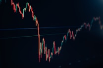 A financial chart displaying a downward trend with multiple sharp peaks and valleys. The chart features predominantly red and green candlesticks against a dark background, indicating fluctuations in market values.