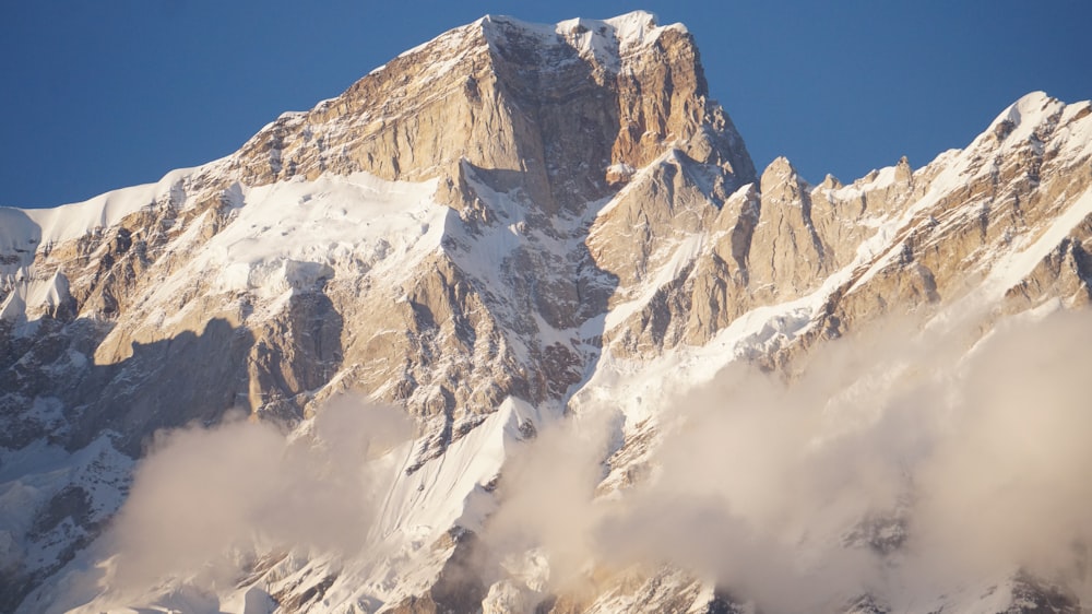 a mountain covered in snow and clouds under a blue sky