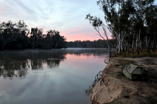 A serene riverside glamping tent nestled among lush green trees at sunset.