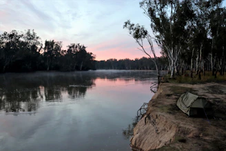 A serene riverside campsite nestled among tall trees at sunset.