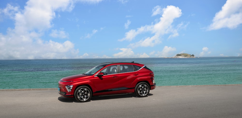 a red car parked on the side of a road next to the ocean