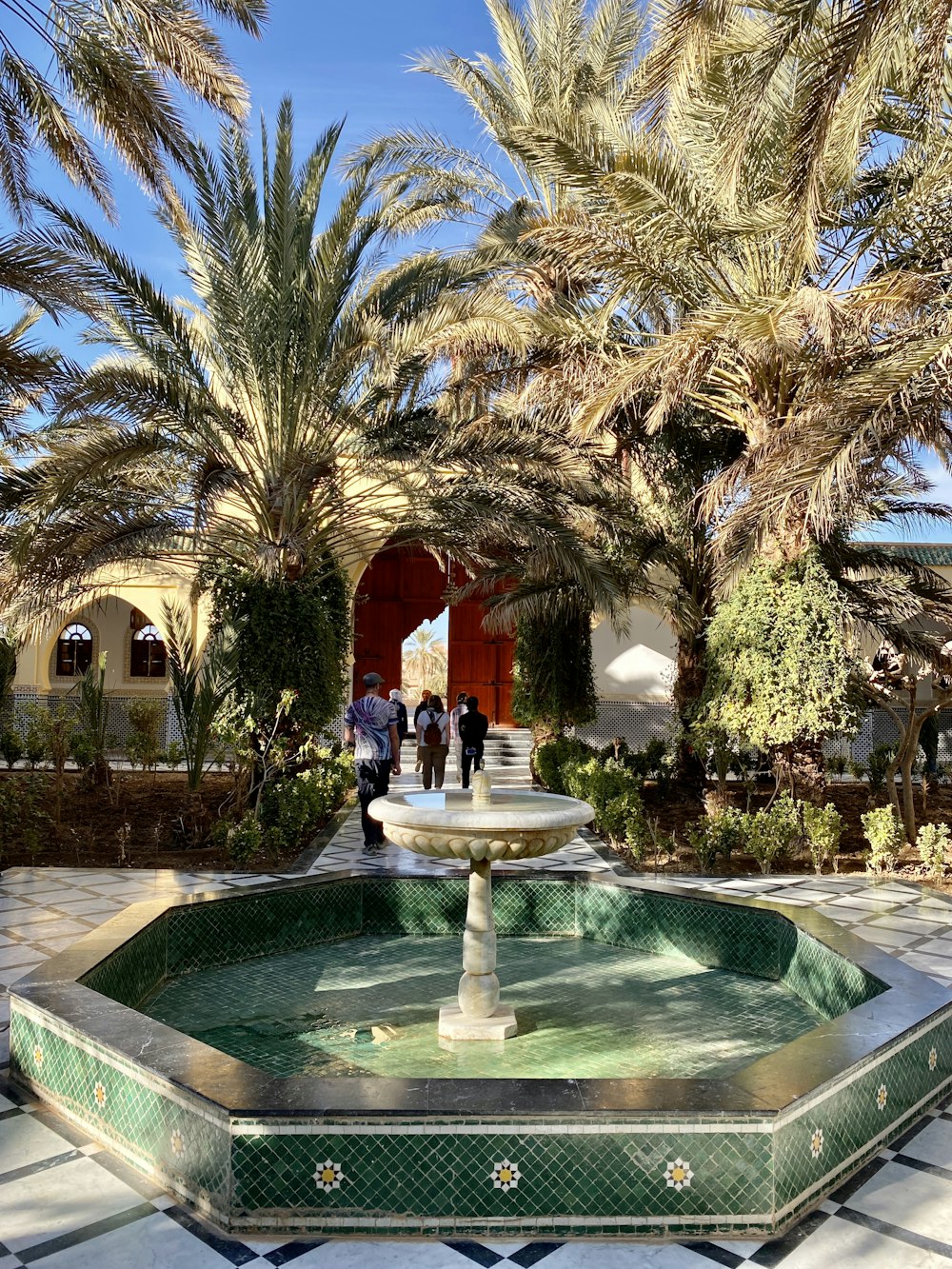 a fountain surrounded by palm trees in front of a building