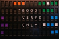 A vintage-style flip board displaying the message 'GOOD VIBES ONLY'. The board features several rows of rectangular panels with a mix of colors, including orange, purple, green, and blue alongside black. Each letter is white against the black background, creating a contrasting visual effect.