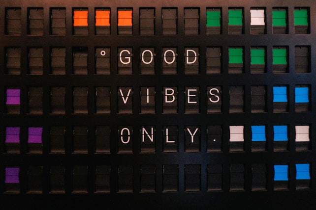 A vintage-style flip board displaying the message 'GOOD VIBES ONLY'. The board features several rows of rectangular panels with a mix of colors, including orange, purple, green, and blue alongside black. Each letter is white against the black background, creating a contrasting visual effect.